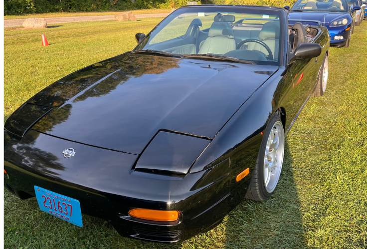 A black 1992 Nissan 240SX Convertible parked on grass, showcasing its sleek design and classic styling.