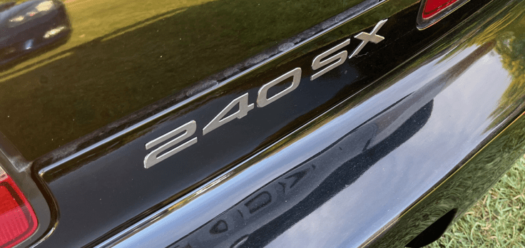 Close-up of the rear badge on a Nissan 240SX convertible, displaying the model name '240SX' on a black surface.