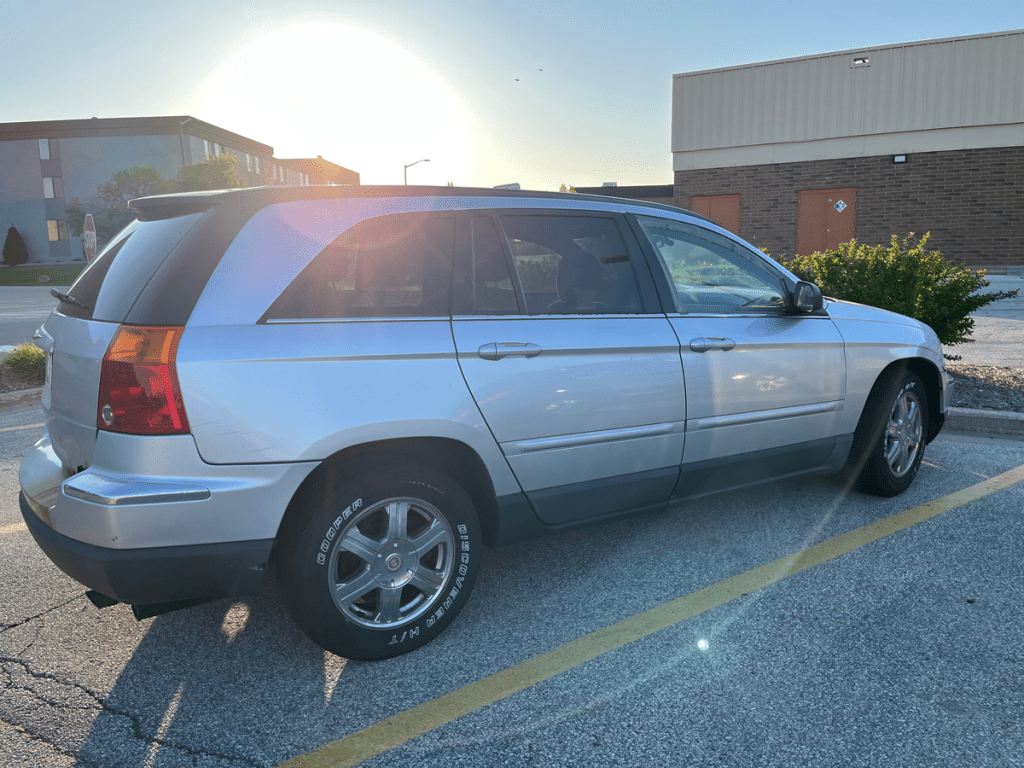 A silver Chrysler Pacifica parked in a lot with a sun flare in the background.