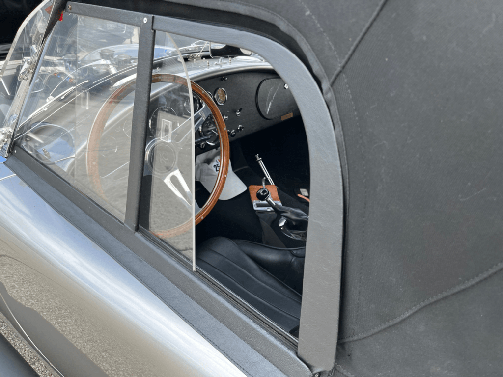 Interior view of a vintage Shelby Cobra showing the steering wheel and dashboard through the driver's side window.