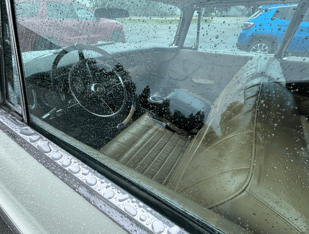Interior view of a vintage Chrysler car with rain droplets on the window, showcasing the steering wheel and leather seats.