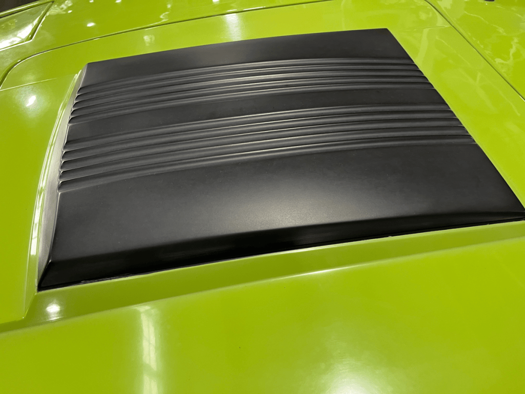 Close-up view of the black engine cover on a vibrant green Saab Sonett III, highlighting its sleek design and textured surface.
