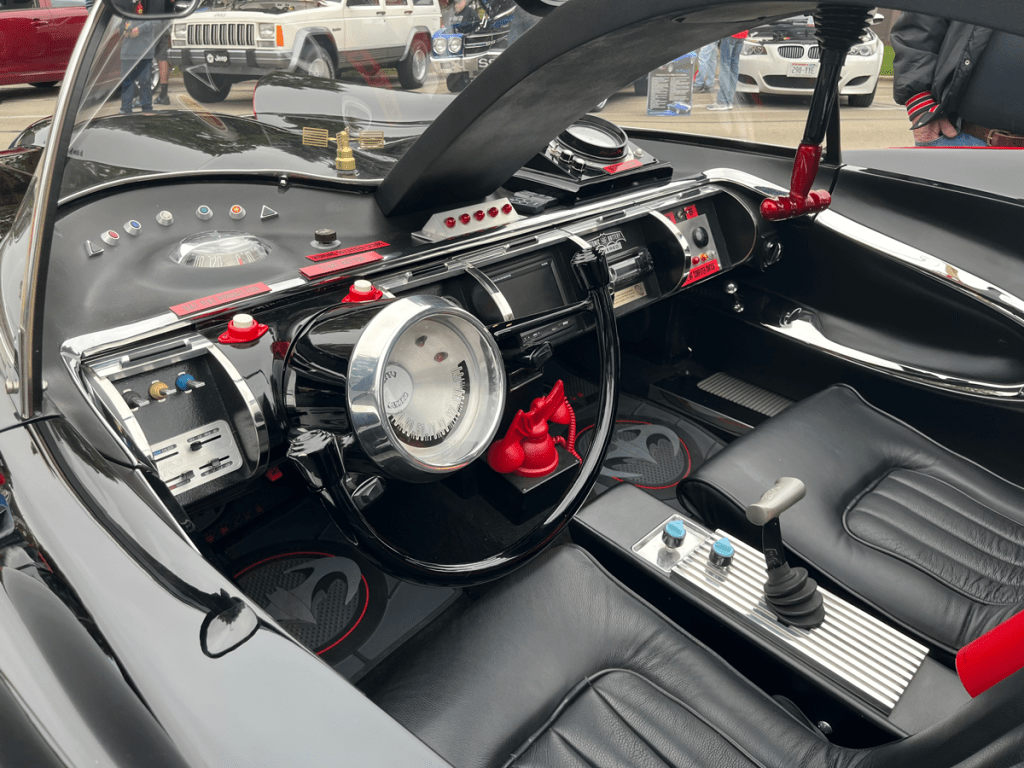 Interior view of a Batmobile replica featuring a detailed dashboard with various controls, a steering wheel, and black leather seats.