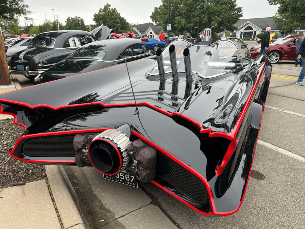 Close-up view of a Batmobile replica featuring its signature sleek design, with prominent fins and tailpipes, displayed at a car show in Green Bay.