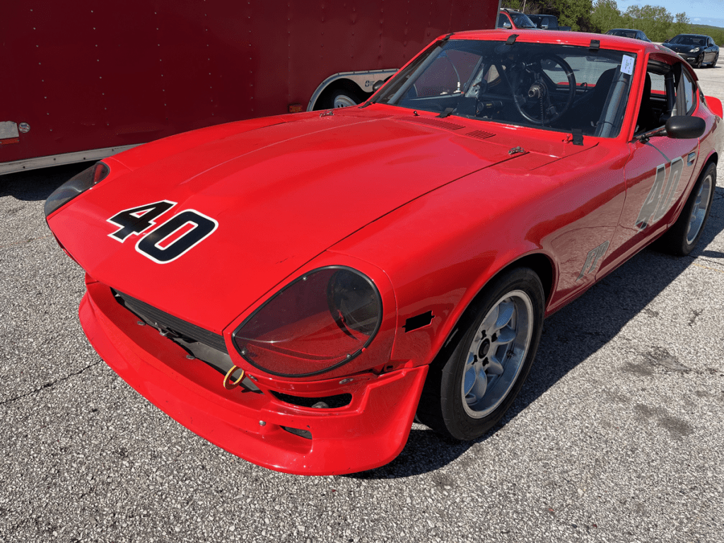 A vintage red Datsun 240Z sports car with the number 40 displayed on its hood, parked in the paddock at Road America.