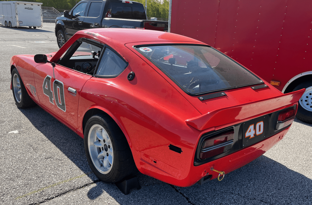 A modified red Datsun 240Z sports car with racing numbers, parked at Road America.