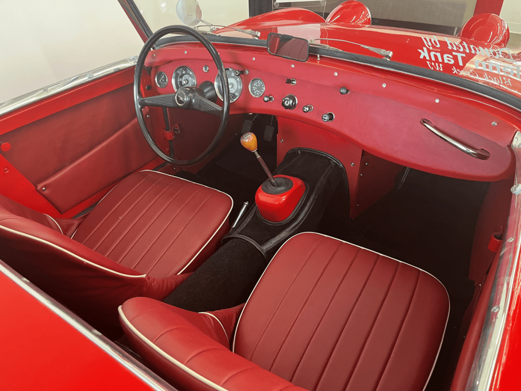 Interior view of a 1958 Austin Healey Bug Eye Sprite featuring red leather seats, a classic steering wheel, and dashboard with vintage gauges.