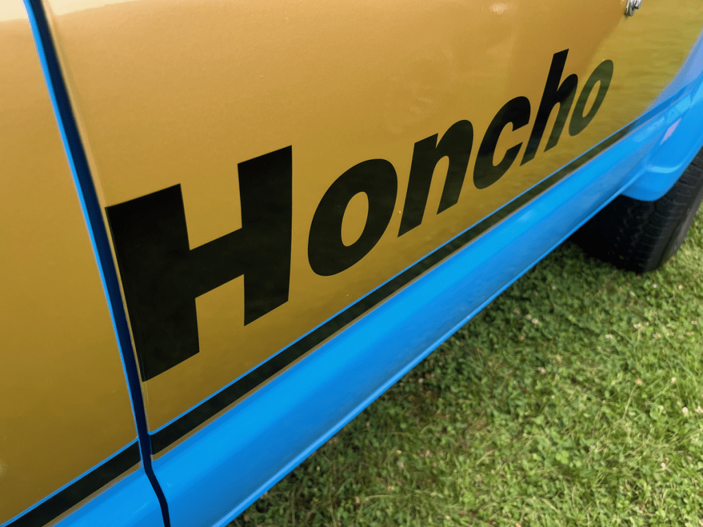 Close-up shot of a Jeep J-10 Honcho side panel featuring the distinctive 'Honcho' decal in black against a gold background.