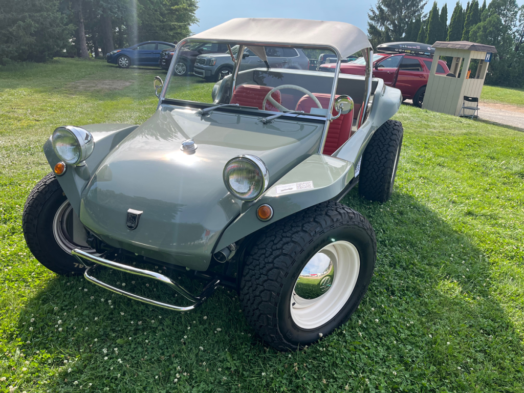 A Meyers Manx Radial Motion 2-seat dune buggy parked on the grass in Oshkosh, showcasing its unique design and shiny exterior.