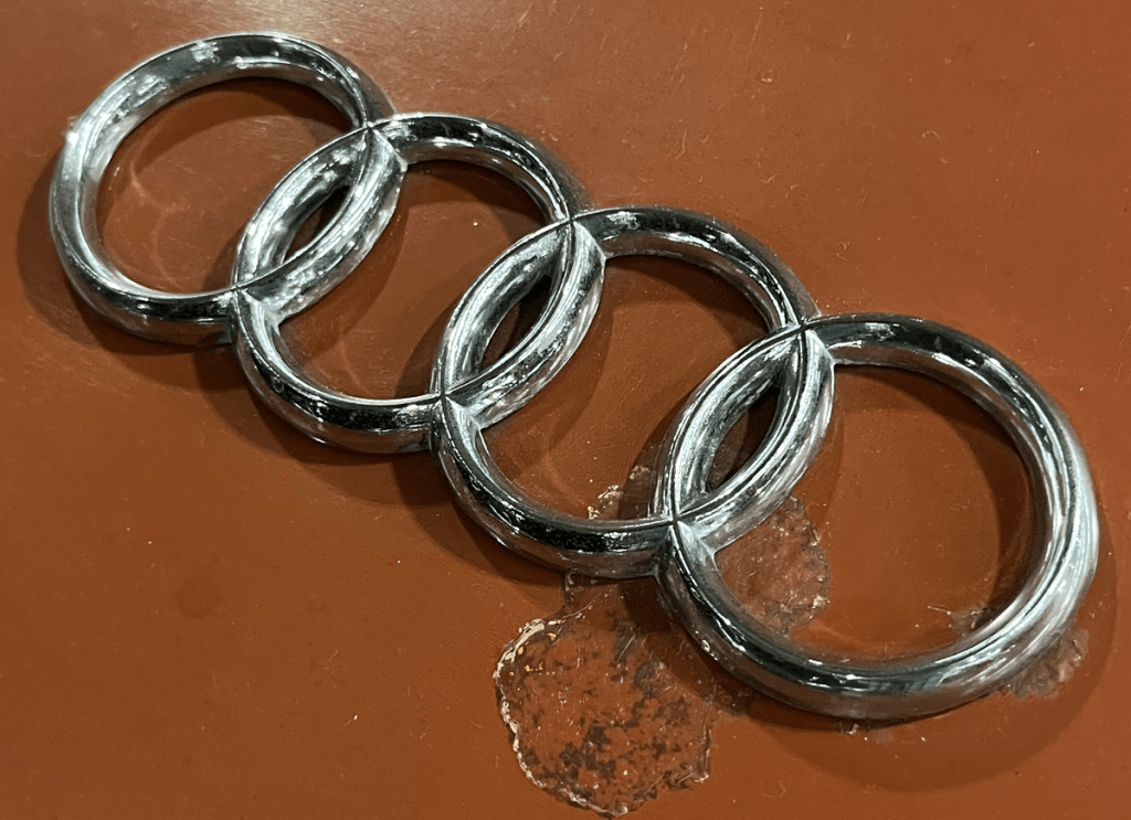 Close-up of the four interlocking rings of the Audi logo on a reddish-brown surface.