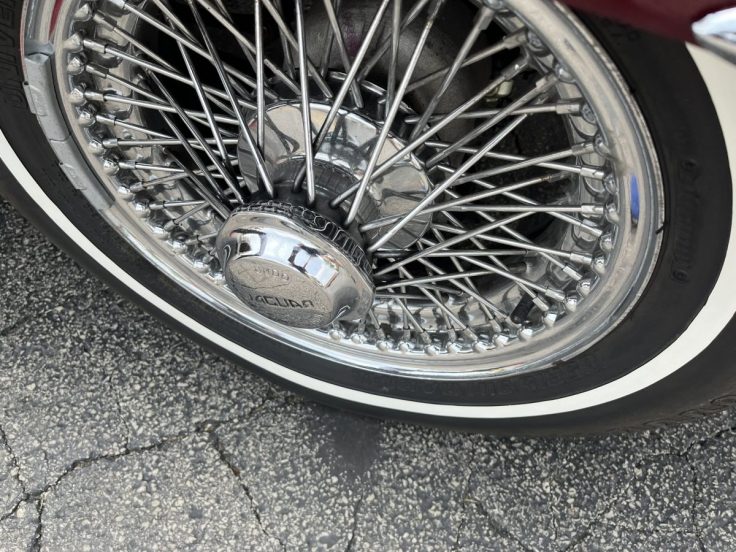Close-up view of a Jaguar E-Type wire wheel featuring a polished chrome hubcap and whitewall tire.