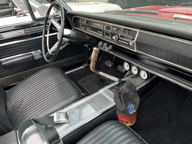 Interior view of a 1967 Dodge Coronet R/T convertible, showcasing black ribbed seats, a classic dashboard with gauges, and a wooden gear shift.