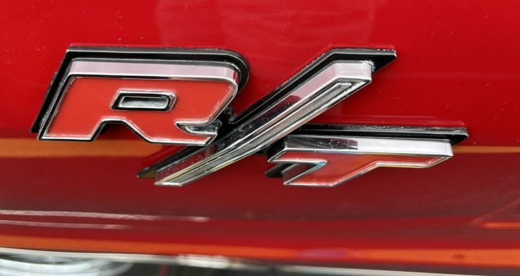 Close-up of the R/T badge on a classic 1967 Dodge Coronet, showcasing its chrome detailing against a red background.