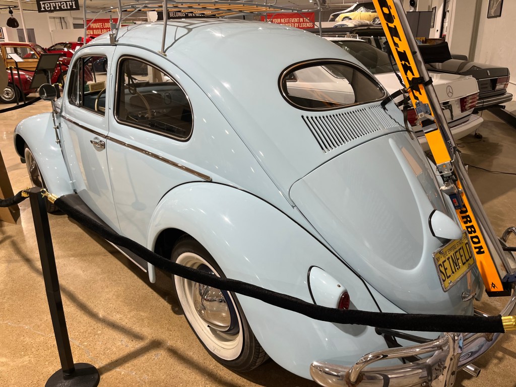 A vintage light blue Volkswagen Beetle on display at Dallas Car  & Toy museum, featuring a ski rack and a 'SEINFELD' license plate.
