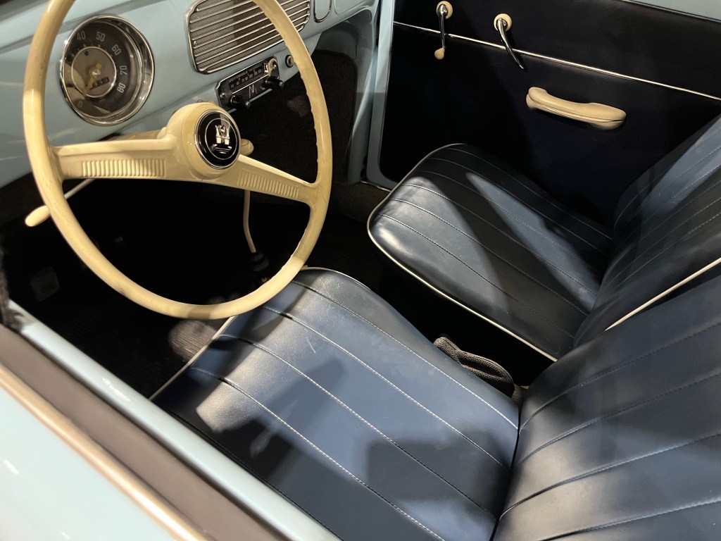 Interior view of a classic blue Volkswagen Beetle, showcasing the steering wheel and upholstered seats.