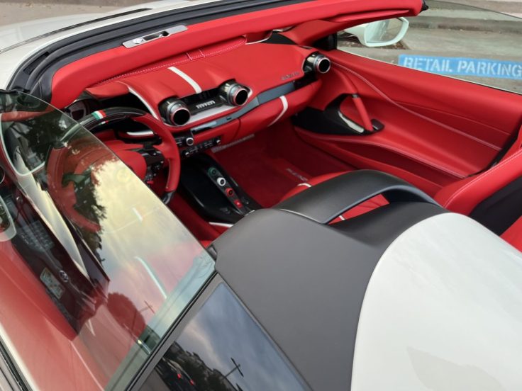 Interior view of a Ferrari 812 GTS featuring a red leather dashboard and seating, showcasing luxurious details and a sporty design.