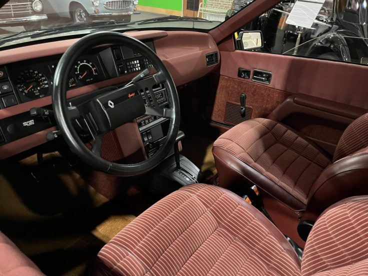 Interior view of a 1985 Renault Fuego, showcasing its burgundy upholstery, steering wheel, and dashboard controls.