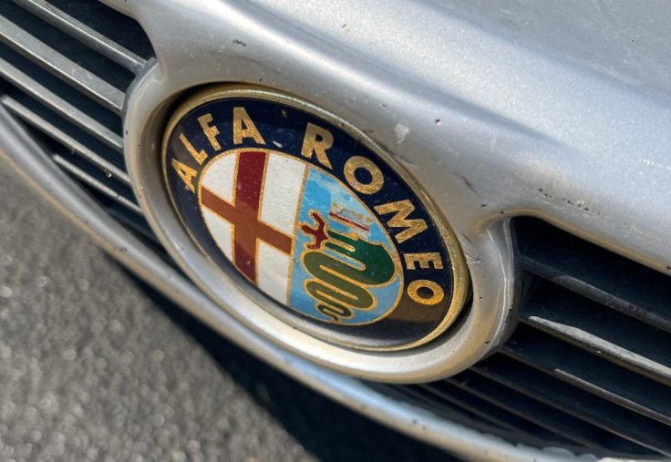 Close-up of the Alfa Romeo logo on a car grille, showcasing the iconic design elements and colors.
