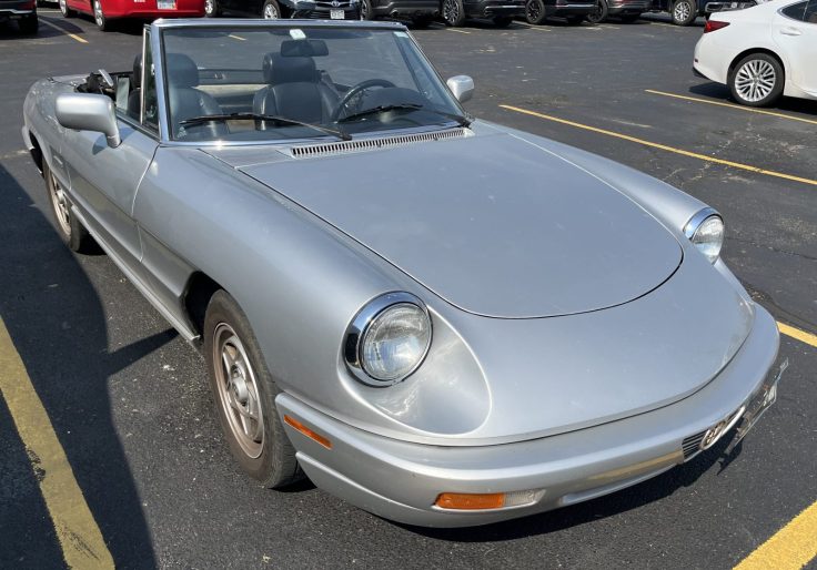 A silver Alfa Romeo Spider Series 4 convertible parked in a lot, showcasing its classic design and front profile.
