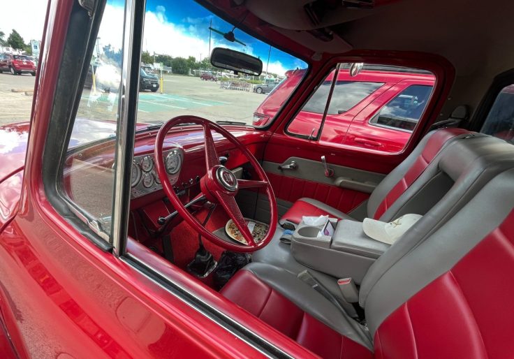 Interior view of a red 1955 Ford F-150, showcasing the steering wheel, dashboard, and seating.