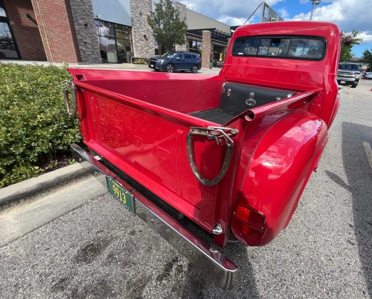 Rear view of a classic red 1955 Ford F-100 truck showcasing its open bed and shiny chrome details.