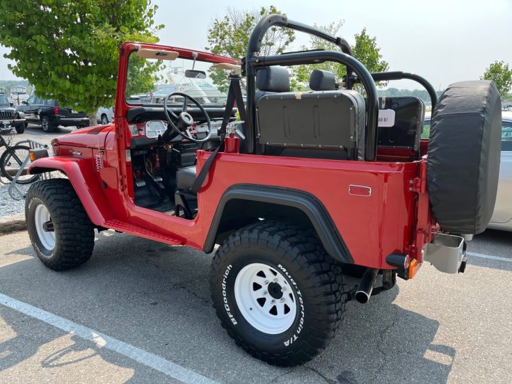 A red 72 Toyota FJ40 with an open top, displaying a spacious interior and rugged tires, parked in a lot with trees in the background.
