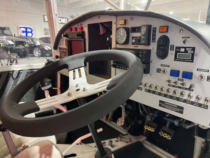 Interior view of a vehicle dashboard featuring a steering wheel, gauges, and various control buttons.
