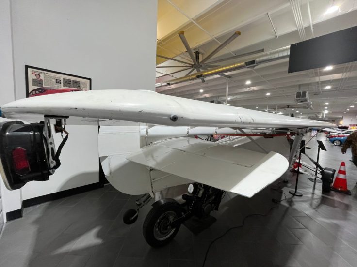 A white aircraft displayed indoors with wings extended, showcasing its design and landing gear.