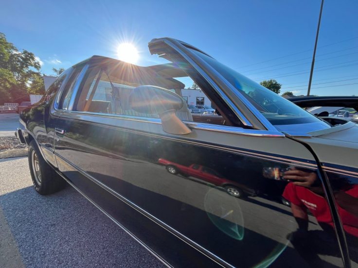 Close-up view of a classic 79 Hurst/ Olds with the roof partially open, parked under sunlight, reflecting the surroundings.