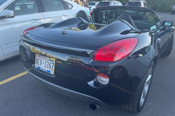 Rear view of a black Pontiac Solstice convertible parked between two cars in a parking lot.