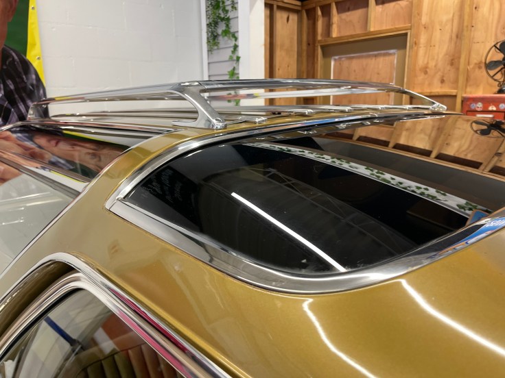 Close-up view of a classic car's roof with chrome detailing and a sunroof, set in a workshop environment.