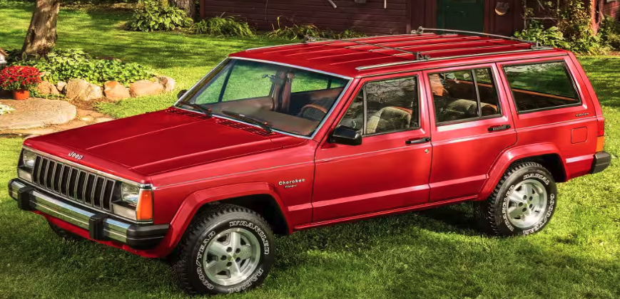 A red 84 Jeep Cherokee parked on green grass, featuring a classic design and a roof rack.