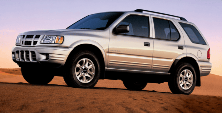 A silver SUV parked on sandy terrain with a clear sky in the background.