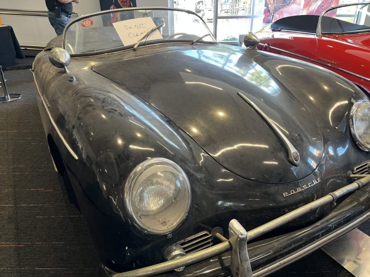 Close-up view of a vintage black Porsche 356 convertible with a dusty exterior, displaying a sign that reads 'Do Not Clean'.