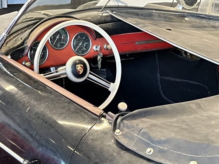 Interior view of a vintage Porsche car showcasing the steering wheel, dashboard with gauges, and red accents.